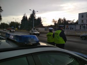 policjanci obserwują ruch pojazdów po drodze publicznej